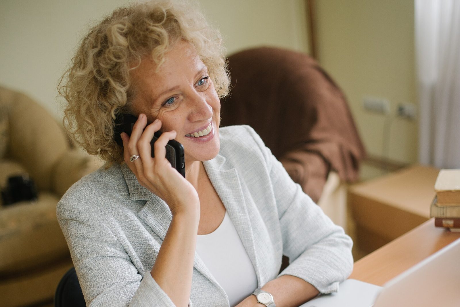 Kvinna som ler och pratar i telefon vid skrivbordet hemma